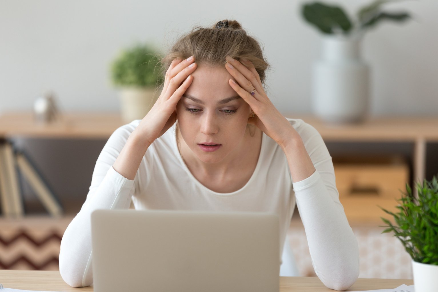 Stressed young woman looking at laptop reading bad internet news